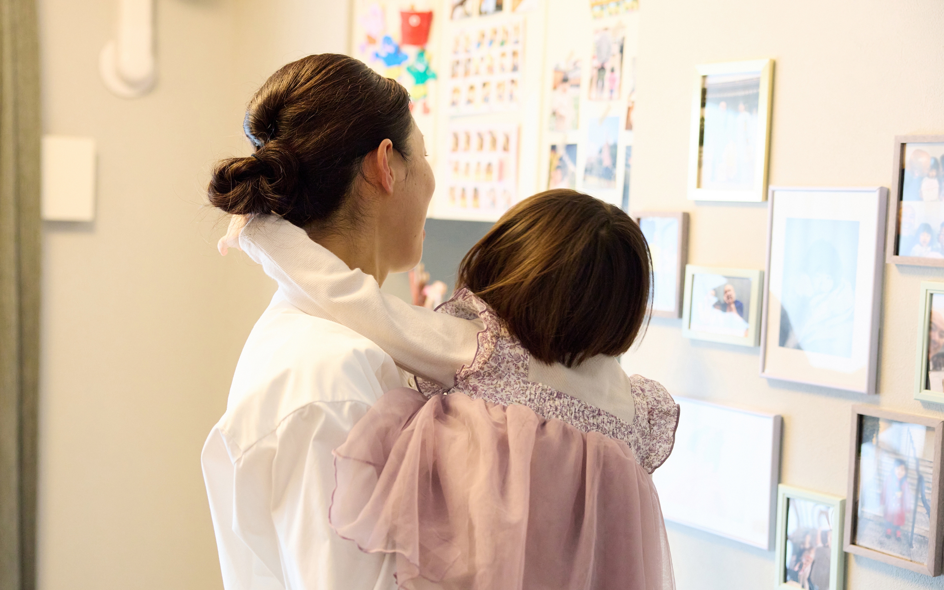 めいちゃんを抱き上げ、壁の写真を見つめる洋子さん